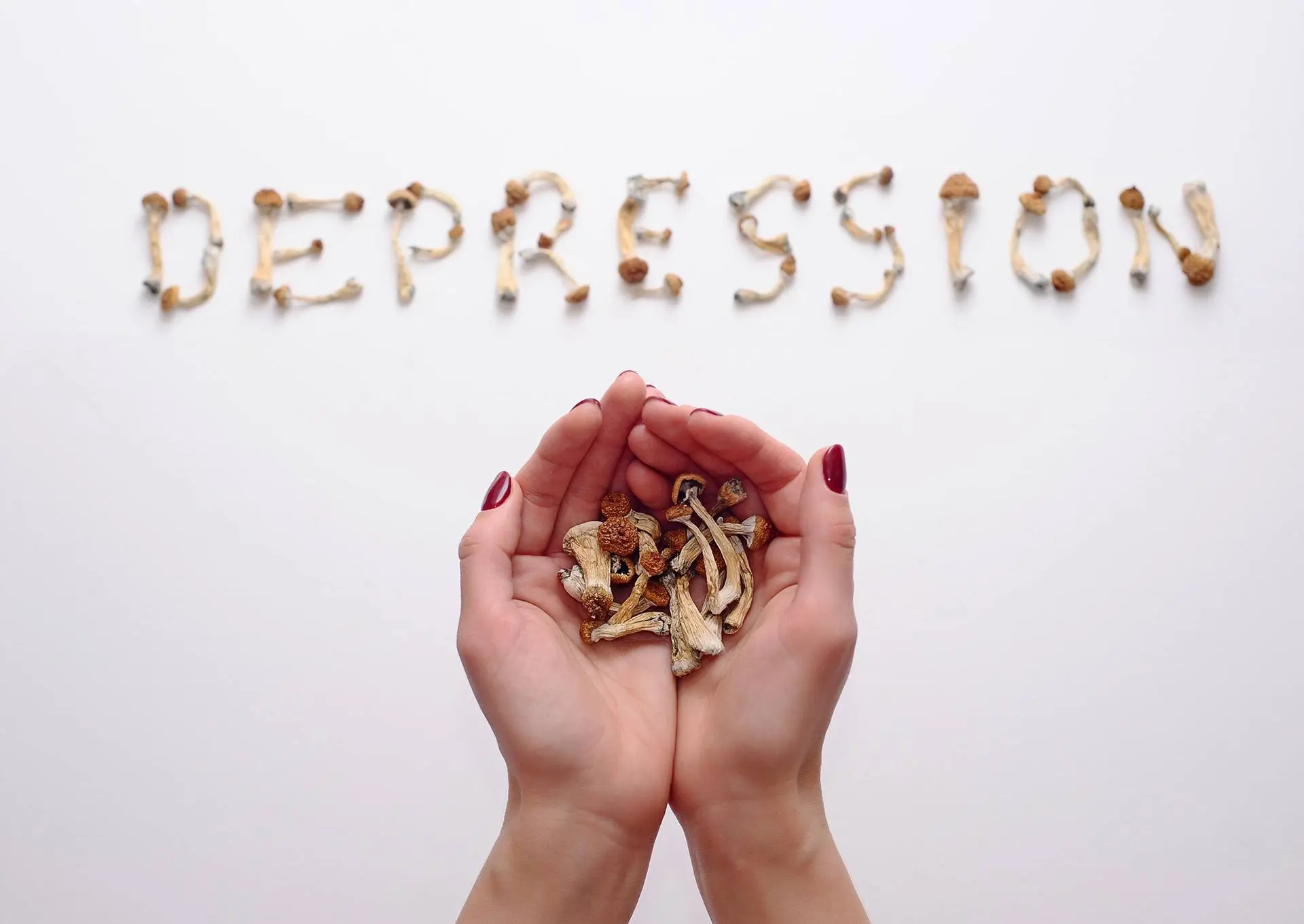 Hands holding psilocybin mushrooms arranged to spell the word 'depression'