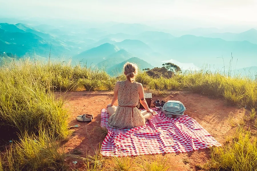 Woman having a picnic and looking at the mountain view, demonstrating one of the most relaxing activities to do while on mushrooms.